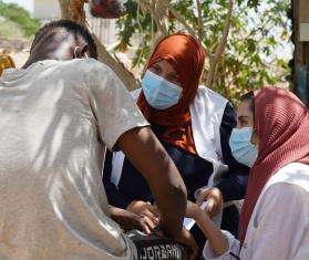MSF staff members wearing face masks, headscarves, and white vests speak to a man with back turned in Libya. 