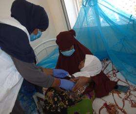 MSF staff member in surgical mask and white vest administers an injection to a baby held by its mother in Somalia.