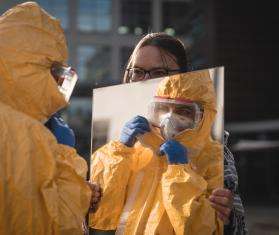 An MSF staff member holds a mirror in front of a person dressed in PPE in Belgium.