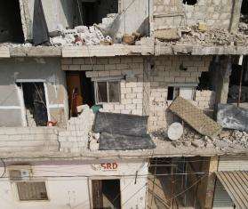A gray concrete building that was damaged by the earthquake with windows blown in and crumbled balconies.