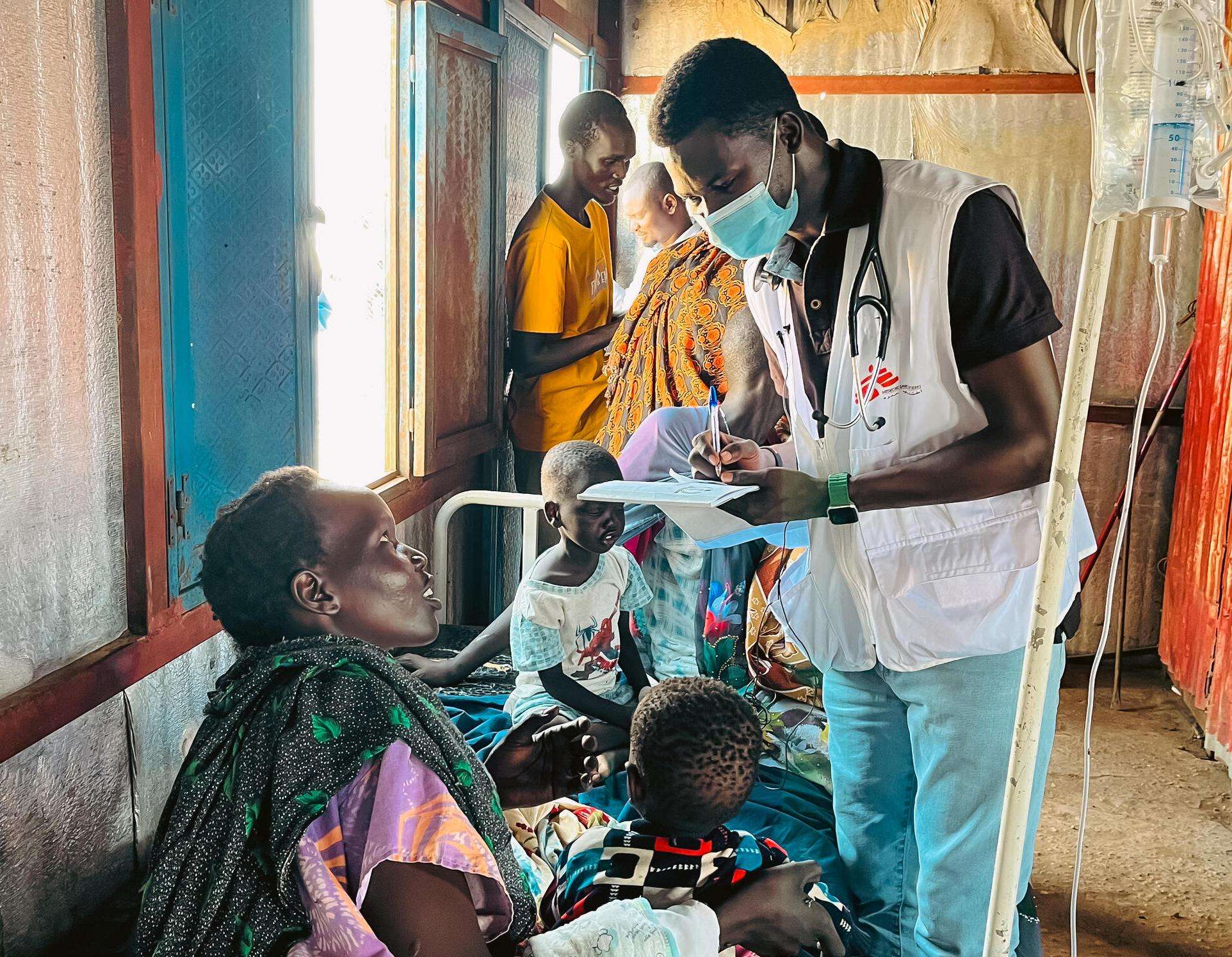 A man in an MSF vest stands over a patient taking notes on his clipboard.