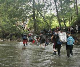 People migrating north walk across a river in the Darién Gap between Colombia and Panama.
