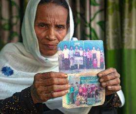 An older woman holds up two photographs of her family members.