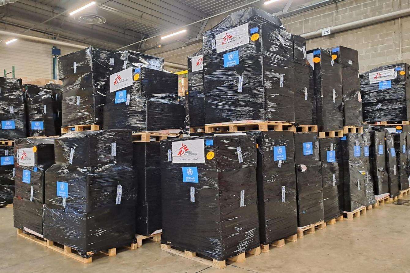 Boxes of medical donations piled on a pallet in a warehouse.