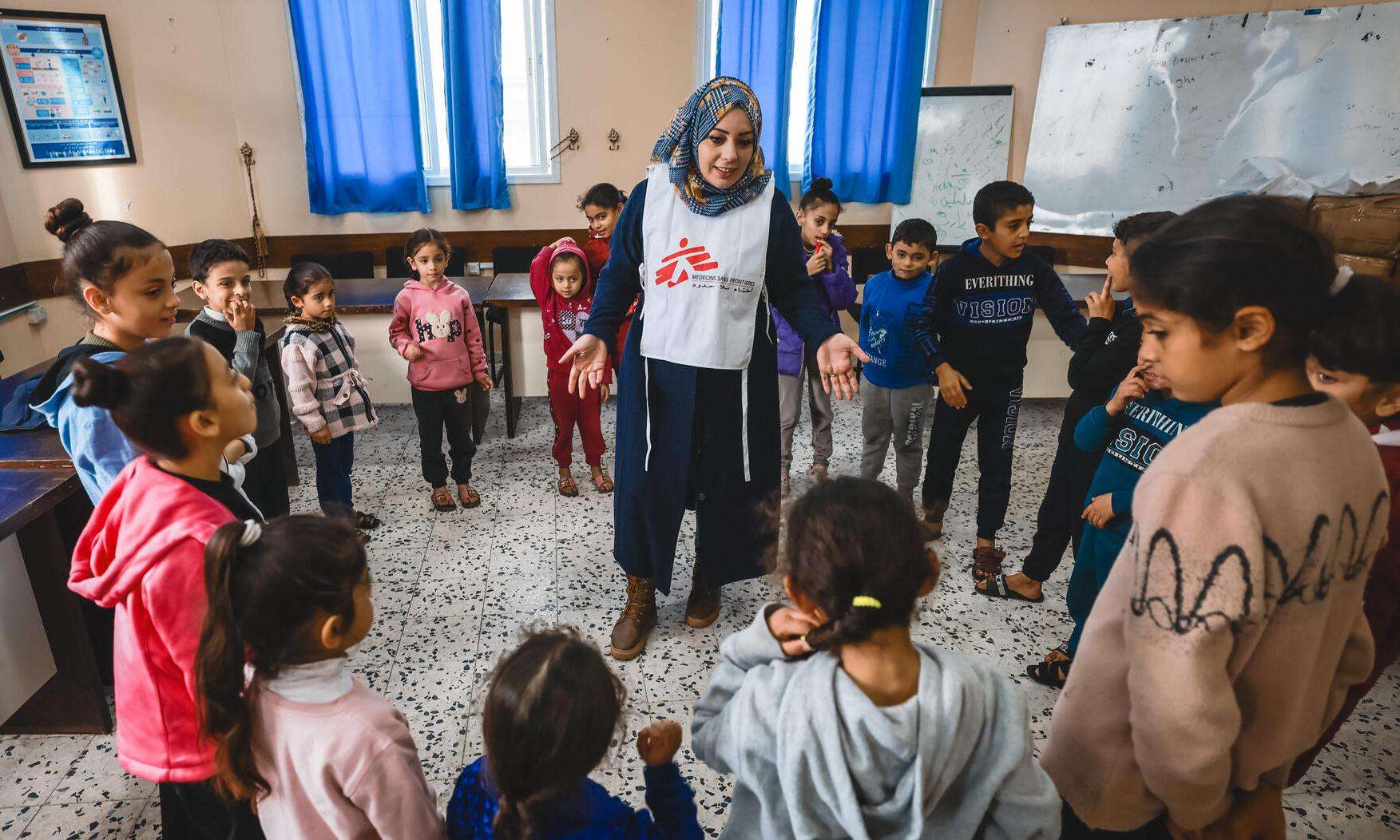 An MSF psychologist stands at the center of a circle of Palestinian children in a mental health session in Gaza.