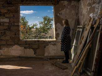 A Ukrainian woman looks out the window of a destroyed building.
