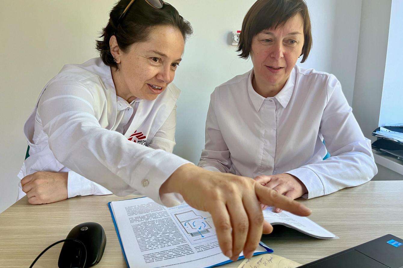 MSF microbiology referent Fabiola Gomez points to an item on a table to a colleague.