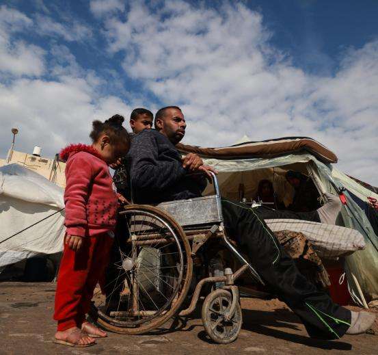 An injured Palestinian man in a wheelchair returns to his tent.