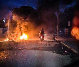 A person rides a motorcycle through fire in Haiti.